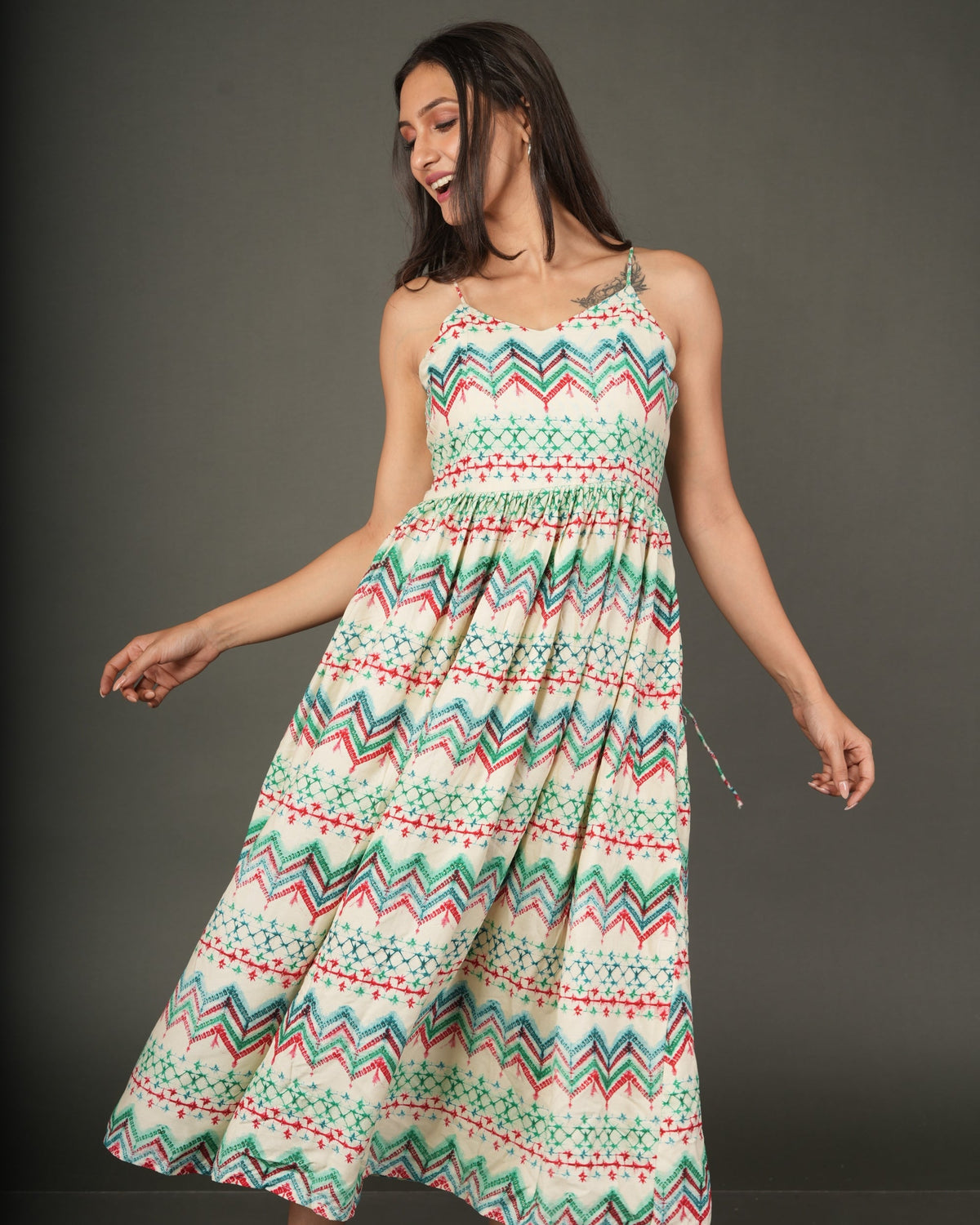 A woman modeling a sleeveless midi dress with a colorful geometric zigzag pattern in green, orange, and white
