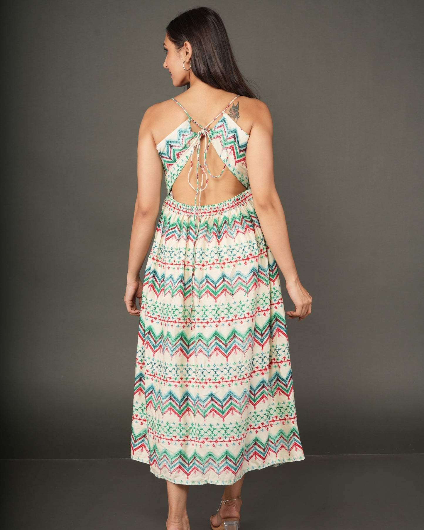 A woman modeling a sleeveless midi dress with a colorful geometric zigzag pattern in green, orange, and white