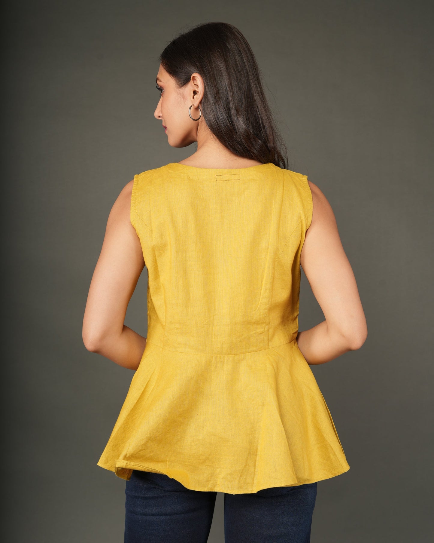 A woman modeling a sleeveless mustard yellow linen-blend peplum top