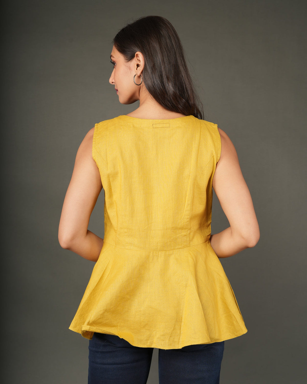 A woman modeling a sleeveless mustard yellow linen-blend peplum top