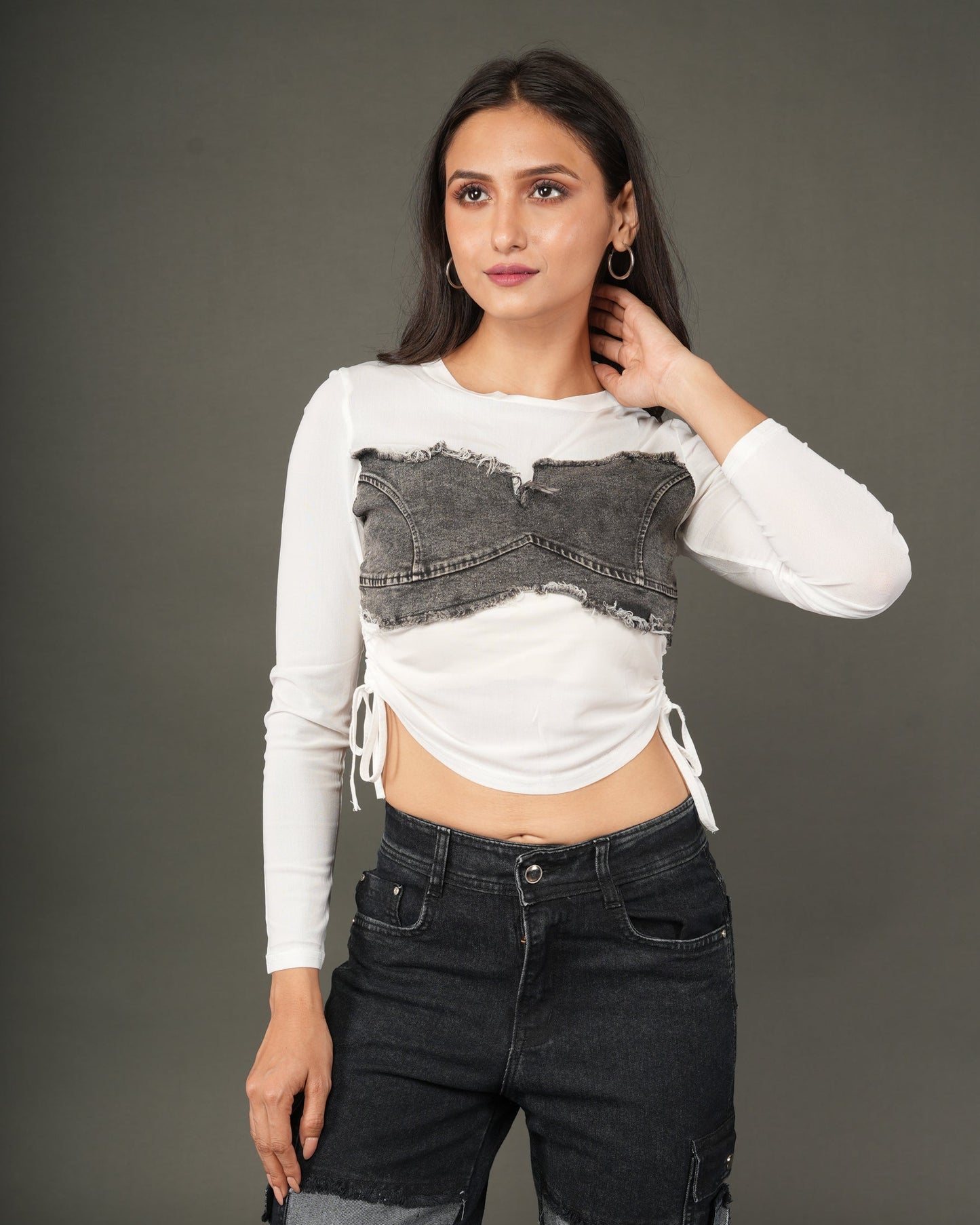 A woman modeling a white long-sleeve crop top with a distressed dark gray denim chest panel