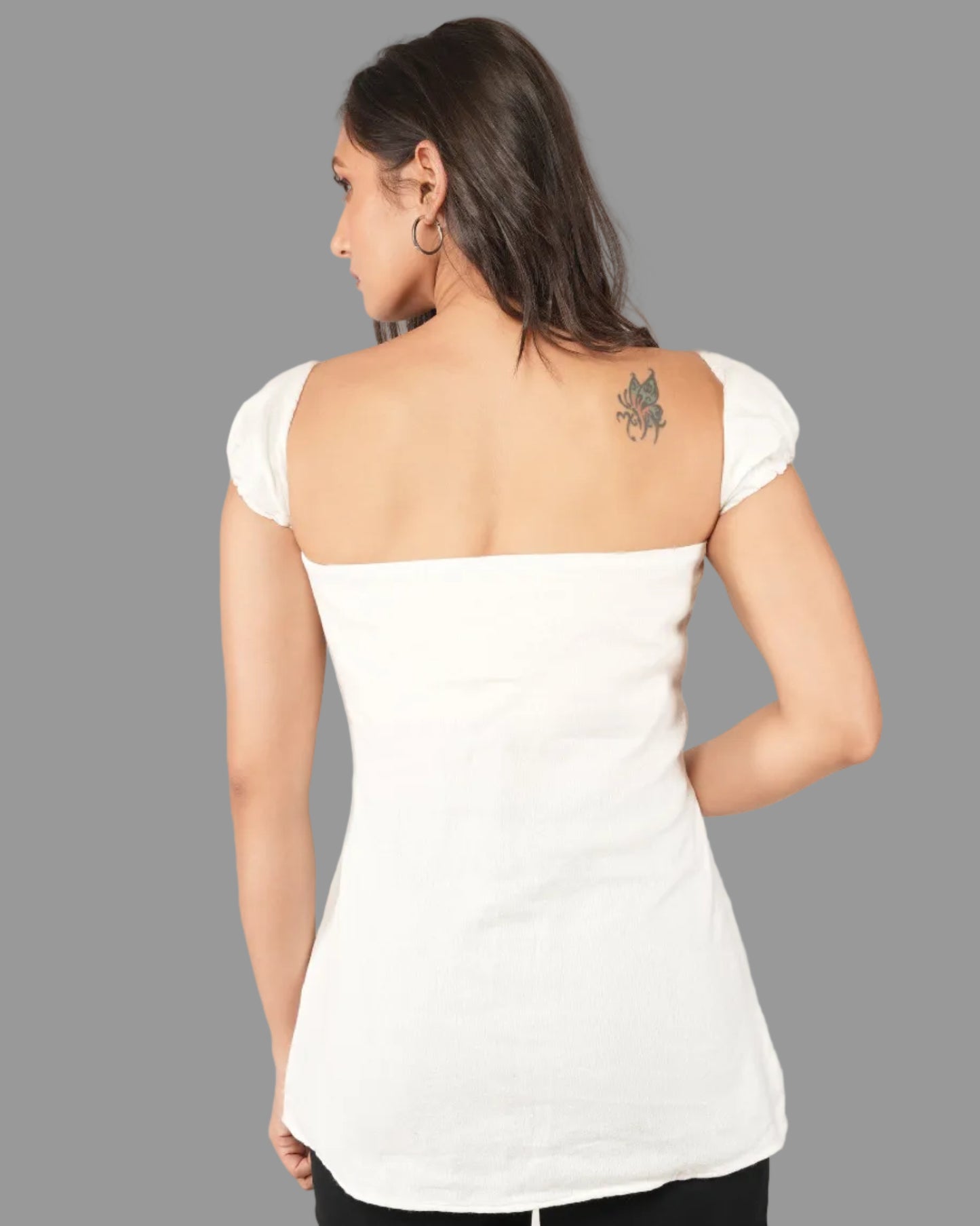 A woman modeling a white short-sleeve top with a ruffled off-the-shoulder neckline and front button placket, paired with black pants.